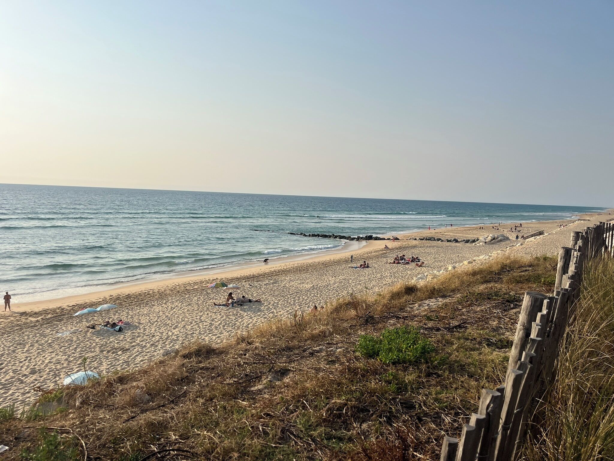 A beach with a wooden fence, sandy shore, and calm sea.