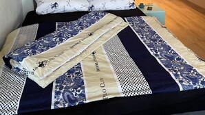 Un dormitorio con cama, cabecera gris y colcha estampada.