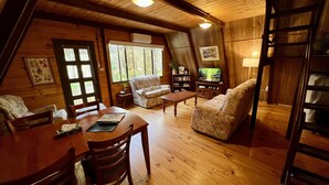 A cozy, wooden cabin interior with a dining table, two sofas, and a ladder.