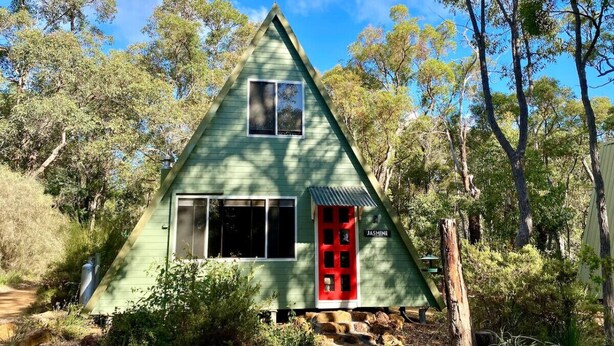 A green triangular house with a red door, surrounded by trees and a clear sky.