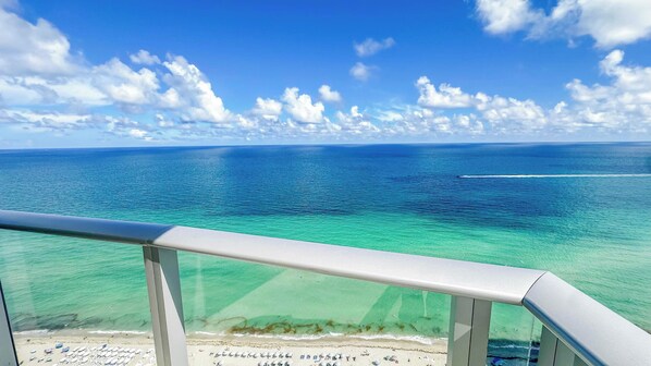 A clear view of the ocean from a balcony with a railing, a sandy beach, and a clear sky. - Opulent Three Bedroom Condo Panoramic Ocean Views (Hollywood)