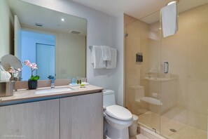 A modern bathroom with a glass-enclosed shower, a white toilet, and a vanity with a mirror and a potted plant. - Opulent Three Bedroom Condo Panoramic Ocean Views (Hollywood)