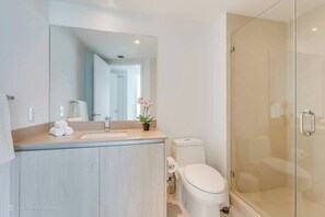 A modern bathroom with a glass shower enclosure, a sink with a mirror, and a toilet. - Opulent Three Bedroom Condo Panoramic Ocean Views (Hollywood)
