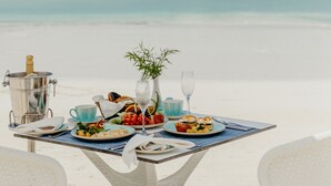 A table set on a beach with a view of the ocean, a drink, and a meal. - LUX Marijani Zanzibar (Pwani Mchangani)