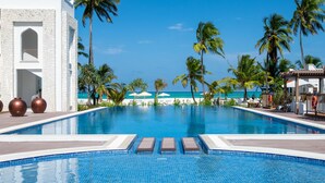 A clear blue pool with lounge chairs, palm trees, and a white building with arched windows. - LUX Marijani Zanzibar (Pwani Mchangani)