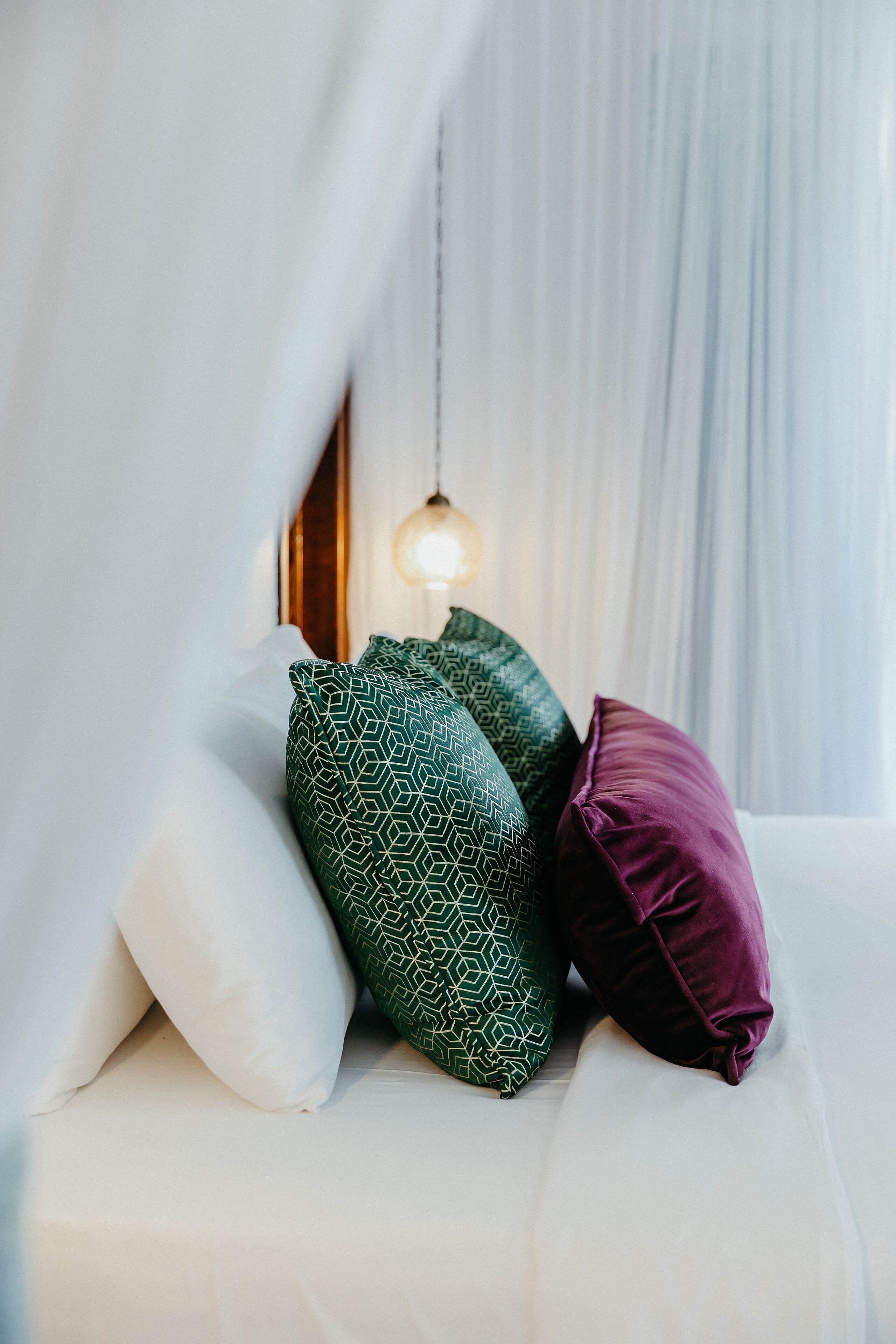 A bed with white bedding and three pillows in different patterns.