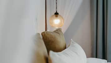Een bed met witte beddengoed en twee kussens, een hanglamp en dunne gordijnen.
