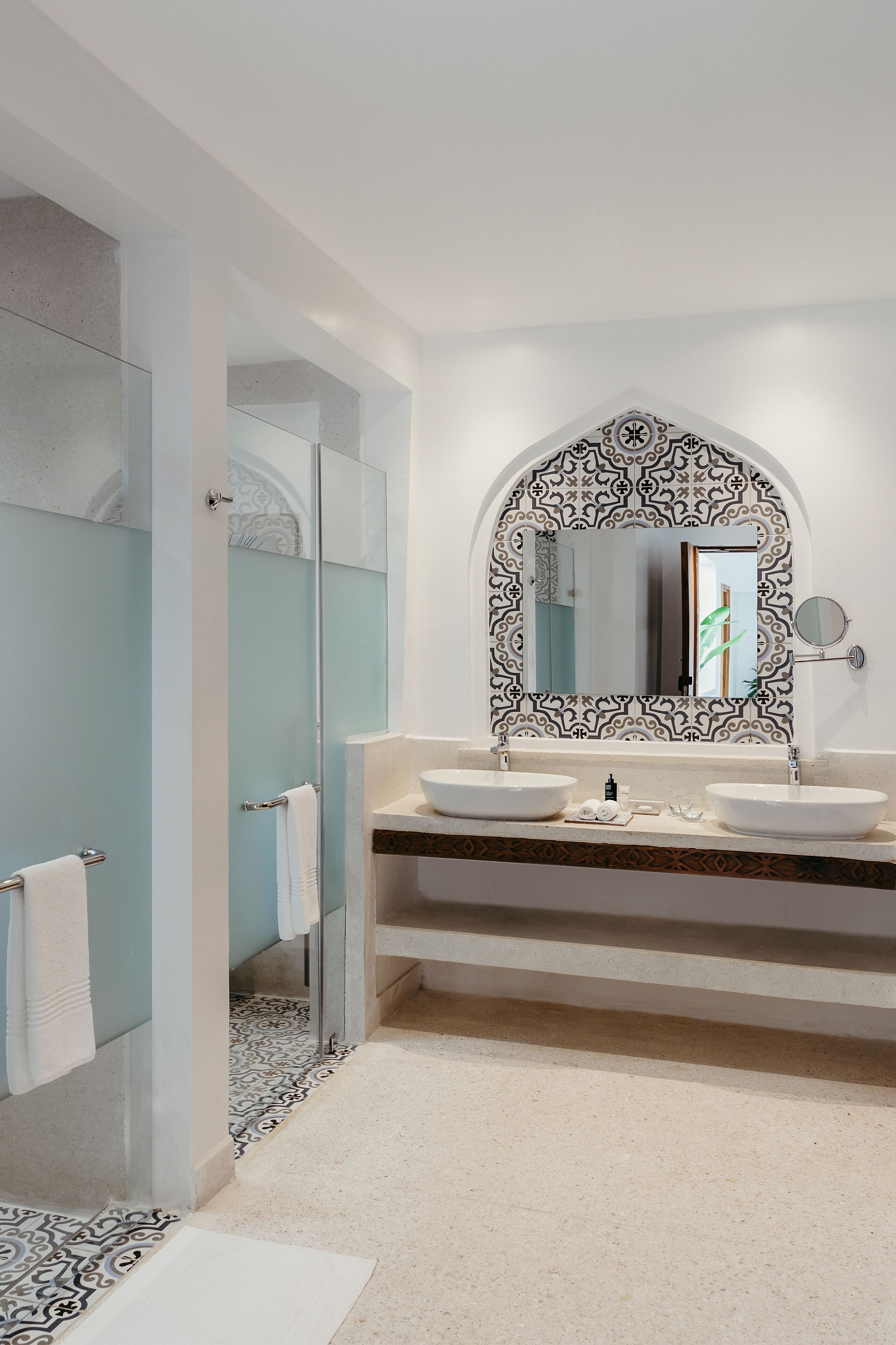 Un baño moderno con un espejo grande, dos lavamanos y una cabina de ducha de vidrio.