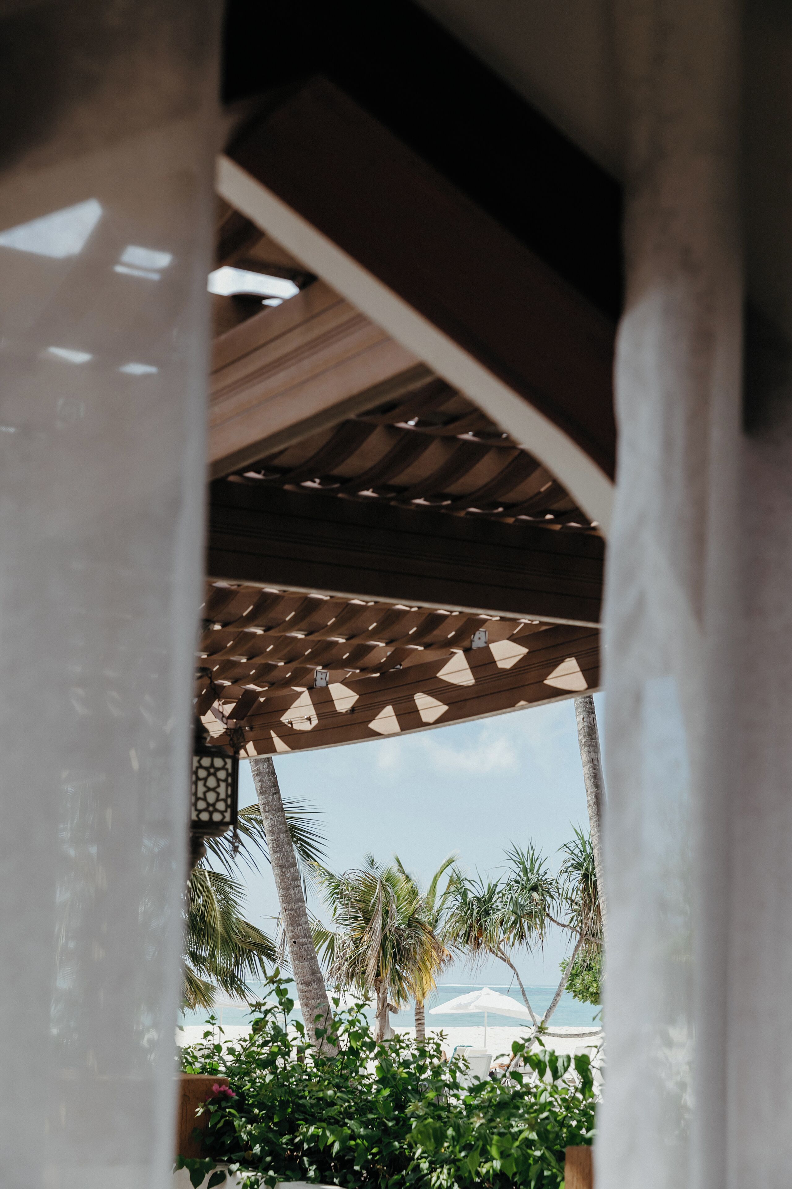 A covered outdoor area with a view of the beach and palm trees.