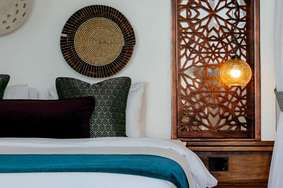 A neatly arranged bedroom with a bed, pillows, a decorative wall panel, and a hanging light fixture.