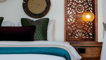 A neatly arranged bedroom with a bed, pillows, a decorative wall panel, and a hanging light fixture.