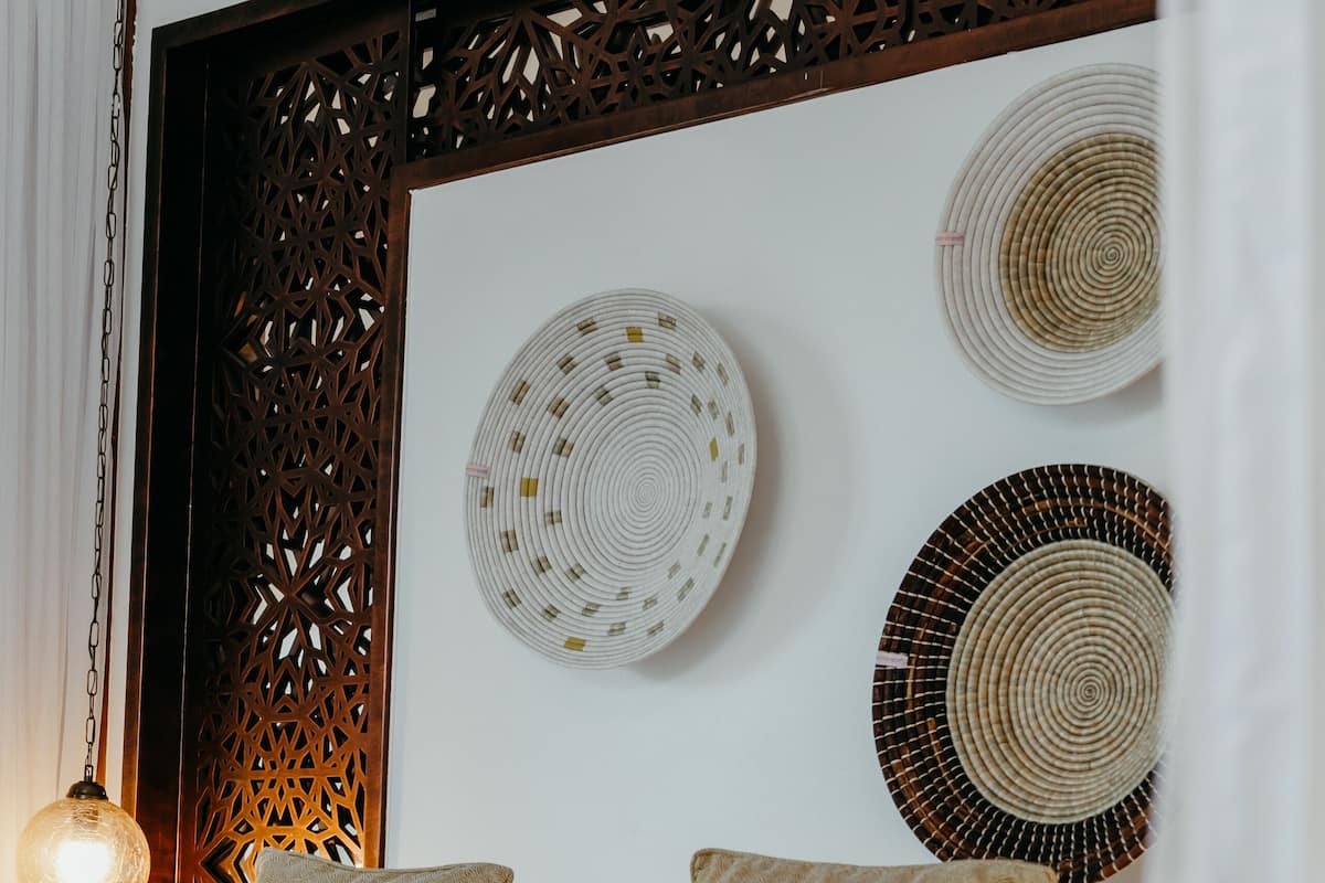 A neatly made bed with white and beige bedding, a hanging light fixture, and decorative woven wall hangings.