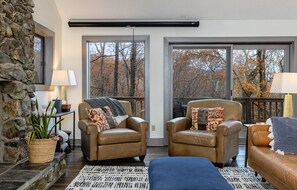 A cozy living room with two leather armchairs, a blue sofa, a stone wall, and large windows with autumn foliage views. - Gorgeous, spacious 4 bedroom home in Wintergreen Resort (Roseland)