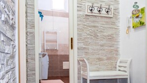 A bathroom with a stone wall, a white bench, and a towel rack. - Spacious and comfortable apartment in Pompeii, pets allowed (Pompei)