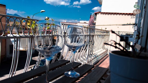 A balcony with metal railings and two empty wine glasses on a wooden table. - Spacious and comfortable apartment in Pompeii, pets allowed (Pompei)