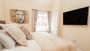 Un dormitorio con cama, almohadas, un cuadro de león, televisor y ventana con cortinas.