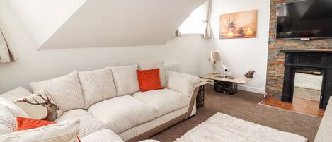 A modern living room with a white sofa, a red pillow, a fireplace, and a TV mounted on a brick wall.