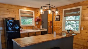 Una cocina con paredes de madera, un refrigerador negro, un lavamanos y una isla de madera con dos taburetes.