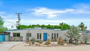 Een laag huis met een blauwe deur, een gevel van natuursteen en een kleine tuin met woestijnplanten.