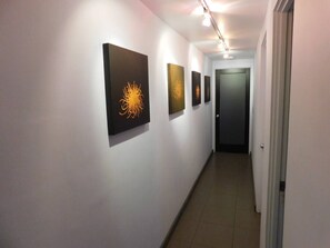 Ein Flur mit vier gerahmten Kunstwerken an den Wänden, einer Tür am Ende und einem gefliesten Boden.