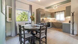 A modern kitchen with stainless steel appliances, a dining area with a round table and chairs, and a view of greenery outside. - Thomas House (Corfu)
