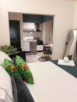 A bedroom with a bed, pillows, a bedside table, a mirror, and a view into a kitchen area with a dining table and chairs. - Beautiful and Cosy Apartment in Patras, Greece (Patras)