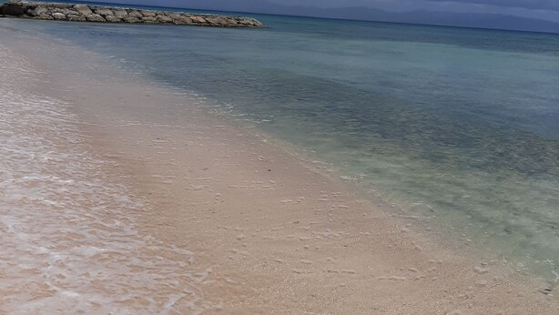 Ein Strand mit klarem Wasser, einem steinernen Wellenbrecher und blauem Himmel.