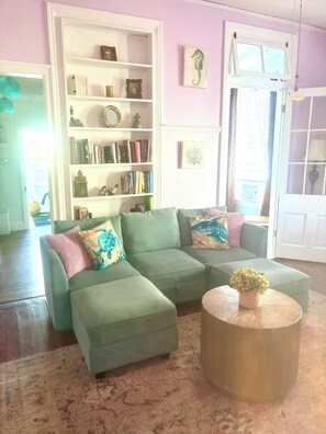 Una sala de estar con un sofá seccional verde, una mesa de centro redonda y una estantería llena de libros y adornos.