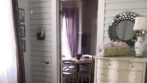 A bedroom with a bed, a dresser, a mirror, and a dining area visible through an open door.