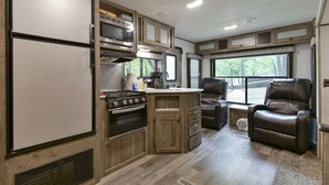 A compact RV kitchen with a refrigerator, stove, microwave, and wooden cabinets. - Givens Glamper Heartland W 3 Beds, Outdoor Pool, Views for Days (Branson)