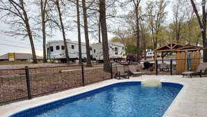 A swimming pool with a wooden deck and lounge chairs, surrounded by trees and RVs in the background. - Givens Glamper Heartland W 3 Beds, Outdoor Pool, Views for Days (Branson)