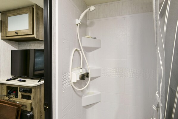 A bathroom with a shower, a vanity with a mirror, and a television.