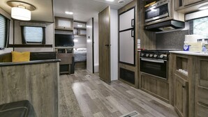 A compact RV kitchen with a stove, microwave, and wooden cabinets. - Givens Glamper Heartland W 3 Beds, Outdoor Pool, Views for Days (Branson)