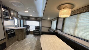 A compact RV interior with a kitchenette, seating area, and a window with blinds. - Givens Glamper Heartland W 3 Beds, Outdoor Pool, Views for Days (Branson)