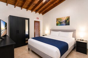 A hotel room with a bed, bedside lamps, a TV, a wardrobe, and an exit sign. - Walk to Beach Luxury 5BR/3BA Villa Hollywood Lakes (Hollywood)
