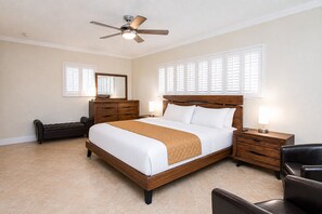 A bedroom with a bed, a wooden dresser, a nightstand, a chair, a ceiling fan, and a window with blinds.