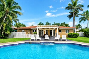 A house with a swimming pool, white fence, and palm trees.