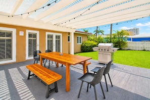 An outdoor patio with a wooden table, chairs, and a grill. - Walk to Beach Luxury 5BR/3BA Villa Hollywood Lakes (Hollywood)