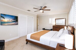 A bedroom with a bed, a ceiling fan, a nightstand, a dresser, a mirror, and a painting of a beach scene.