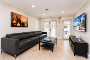 A modern living room with a black leather sofa, a coffee table, and a flat-screen TV mounted on the wall.