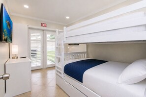 Une chambre d’hôtel avec un lit superposé, un bureau avec une lampe, un panneau de signalisation indiquant la sortie et un téléviseur.