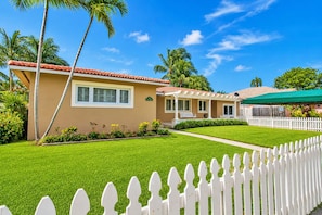 A residential property with a well-maintained lawn, a white picket fence, and a two-story house with a red-tiled roof. - Walk to Beach Luxury 5BR/3BA Villa Hollywood Lakes (Hollywood)