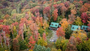 An aerial view of a cabin surrounded by a dense forest with autumn foliage.