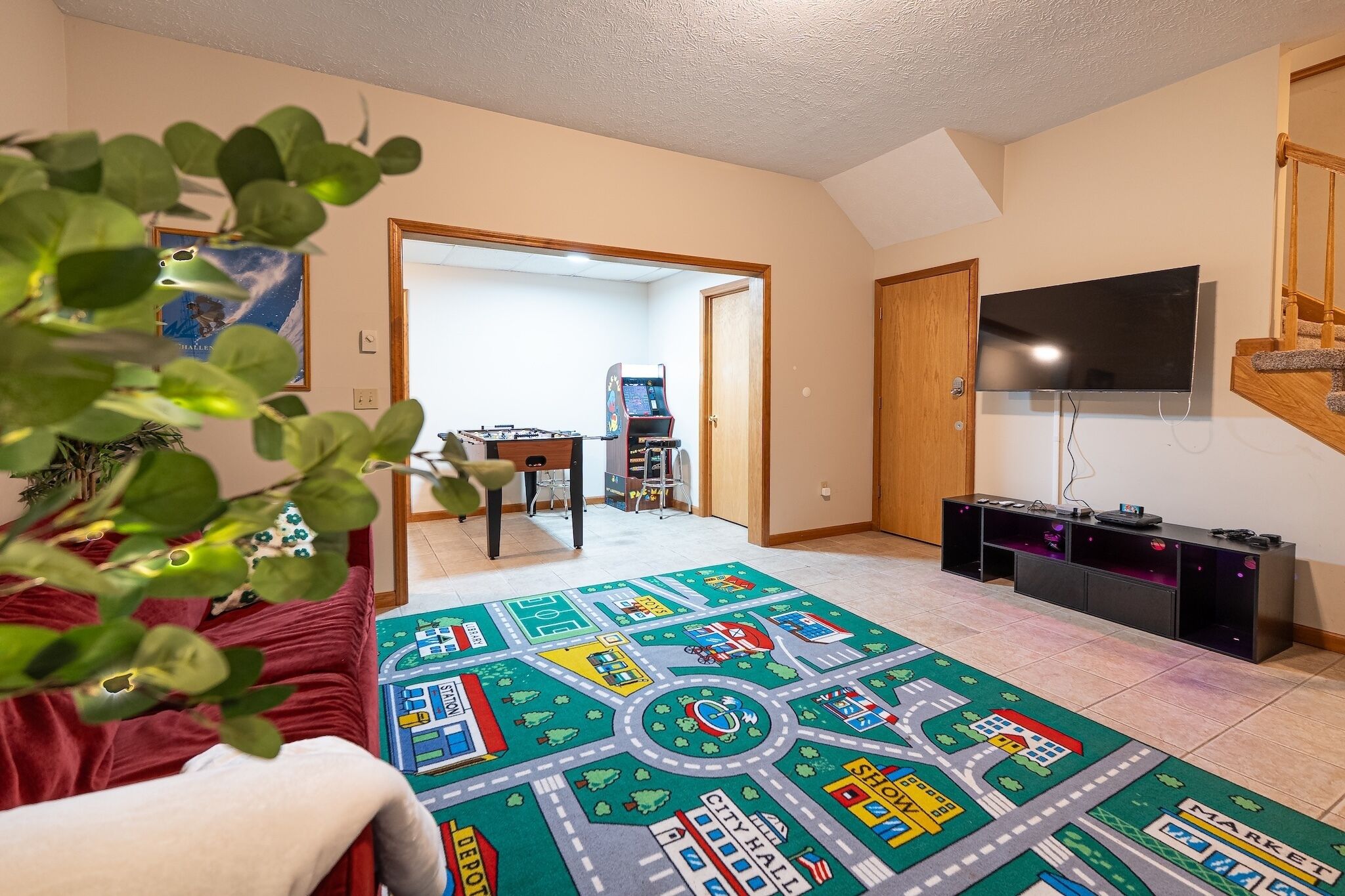 Een woonkamer met een rode bank, een groen-wit kleed, een flatscreen televisie en een houten kast.