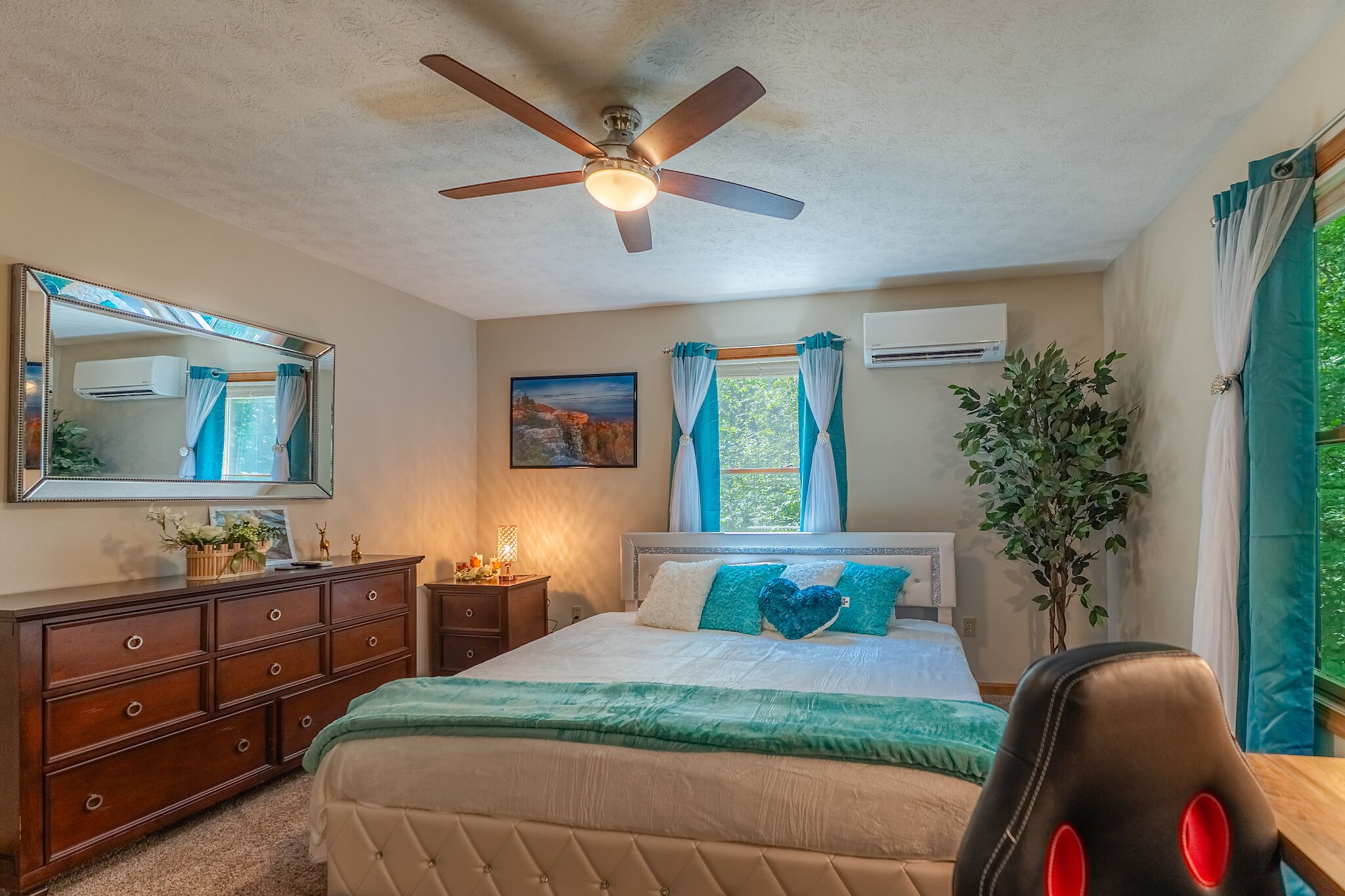 A bedroom with a bed, dresser, ceiling fan, and a potted plant.