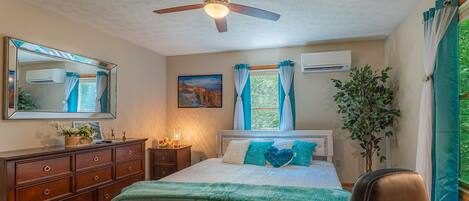 A bedroom with a bed, dresser, ceiling fan, and a potted plant.