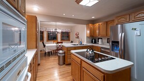 A modern kitchen with wooden cabinets, a stainless steel refrigerator, a built-in oven, and a dining area with a table and chairs.