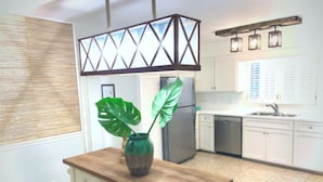 Une cuisine avec un îlot central en bois, un réfrigérateur, des armoires blanches et un luminaire suspendu.