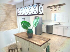 A kitchen with a wooden island, a refrigerator, white cabinets, and a hanging light fixture.