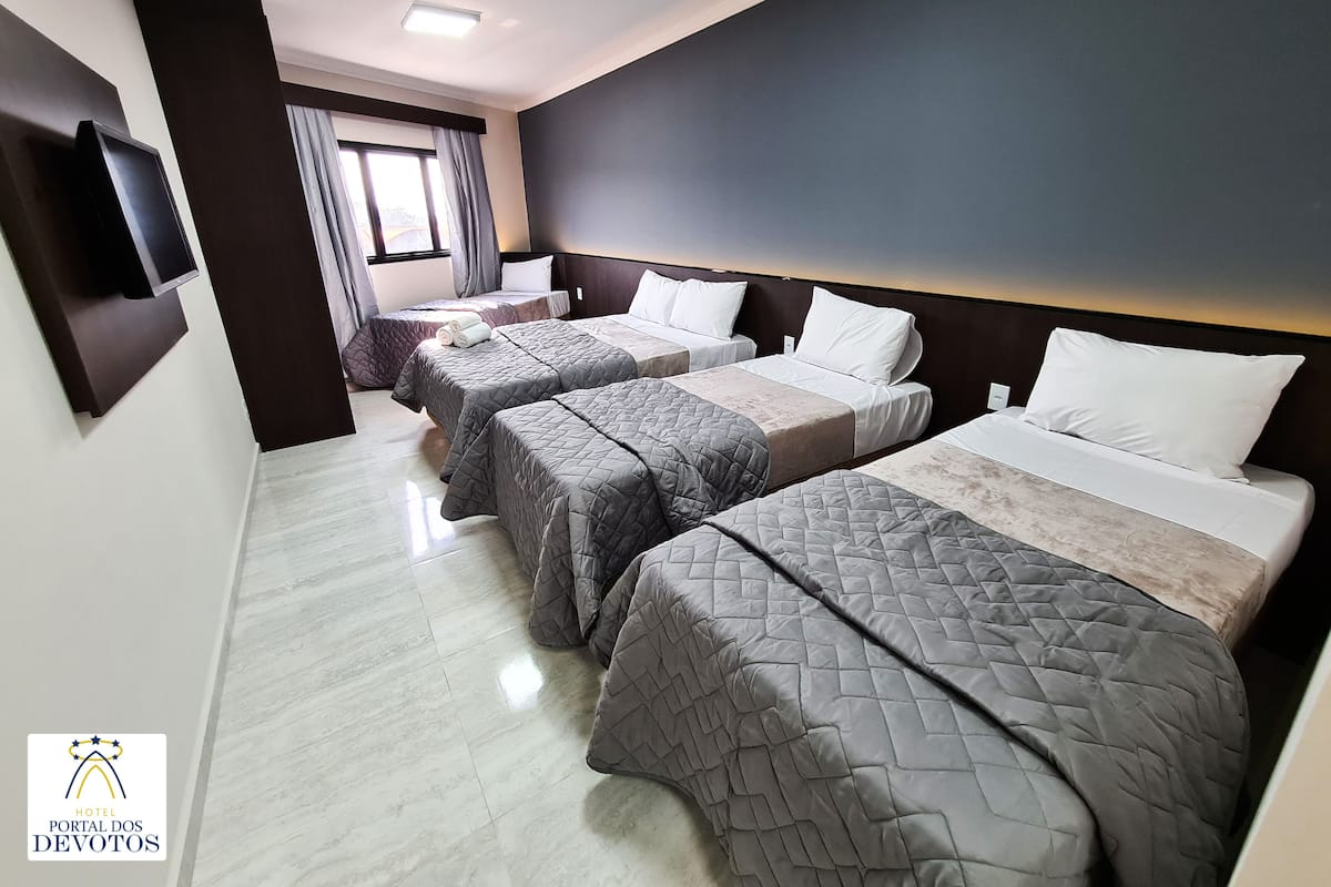 A hotel room with three beds, a flat-screen TV mounted on the wall, and a window with curtains.
